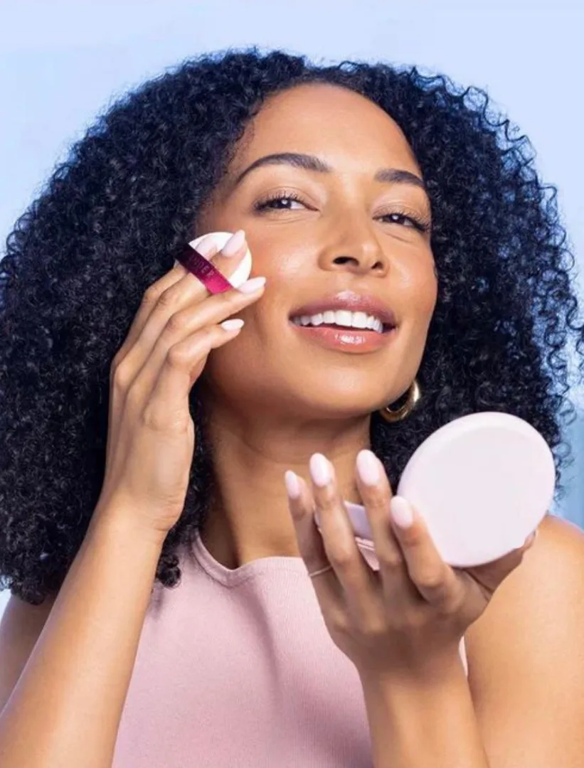 A young woman applying powder with a puff while holding a compact